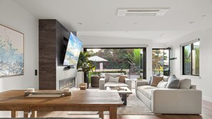 A modern living room with a fireplace, a large TV, and a view of the outdoors. - NEW: Fun on 4th Encinitas (Aug 2026) rooftop fire pit (Encinitas)