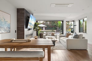 Ein modernes Wohnzimmer mit Kamin, großem Fernseher und Blick ins Freie.