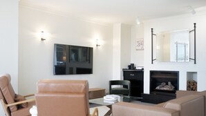A modern living room with a flat-screen TV, a fireplace, and two armchairs. - The Penthouse | Spa, Sauna, Gym, 360° Views, 4BR (Glenelg North)