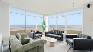 A spacious living room with large windows, a green sofa, a black leather couch, and a coffee table. - The Penthouse | Spa, Sauna, Gym, 360° Views, 4BR (Glenelg North)