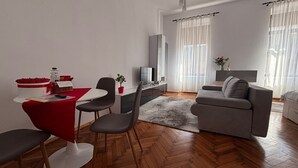 Una sala de estar moderna con comedor, un sofá gris, un televisor y una silla roja.
