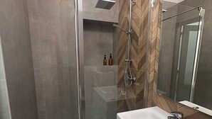Un baño moderno con ducha envuelta en vidrio, un lavamanos blanco y pared con patrón de espiga.