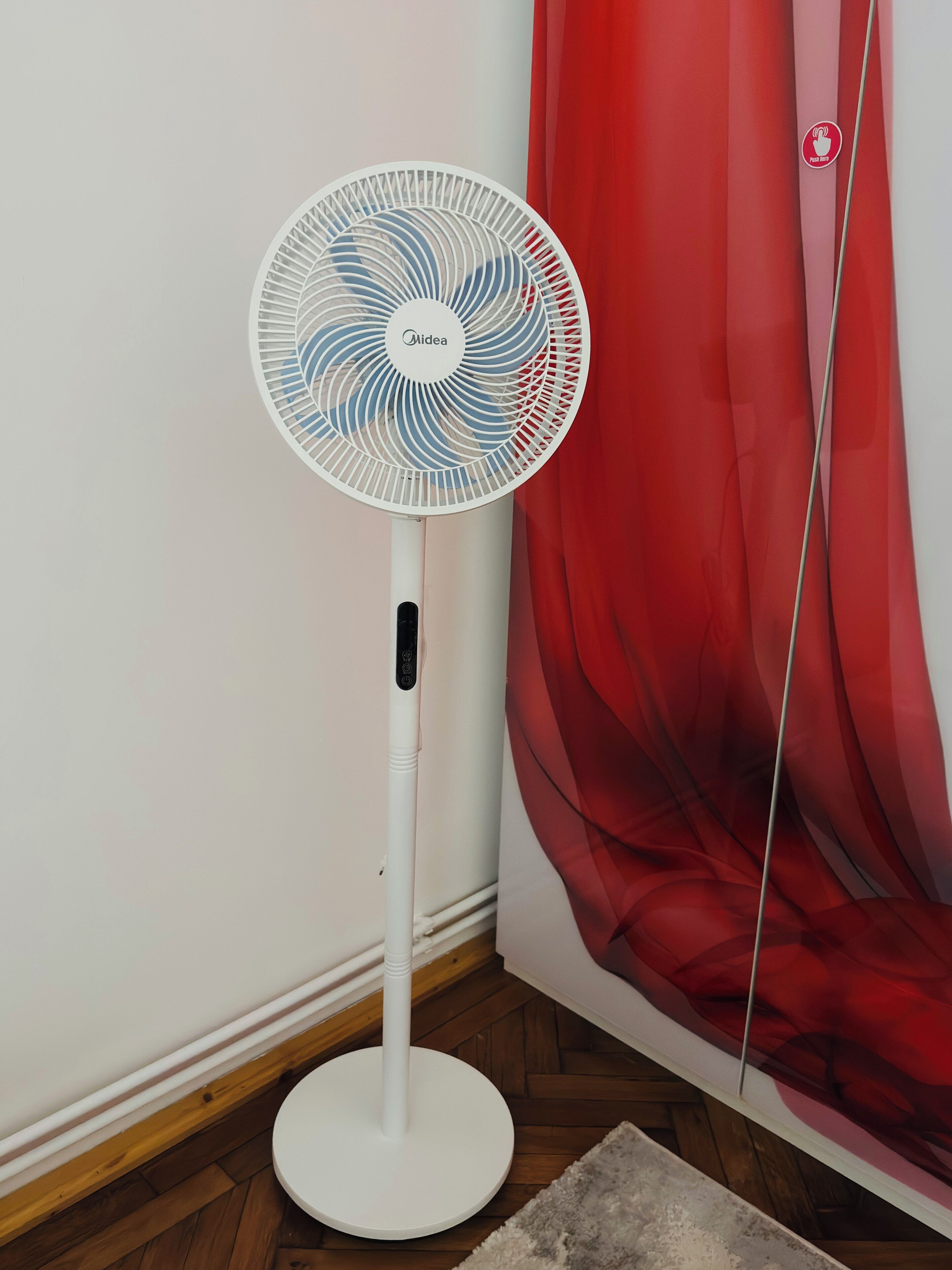 A standing fan with a control panel, positioned near a red curtain.