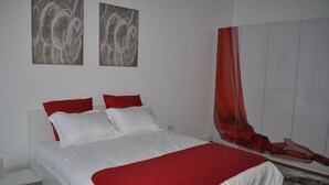 Un dormitorio con una cama, una mesita de noche, una manta roja y blanca, y dos cuadros abstractos en la pared.