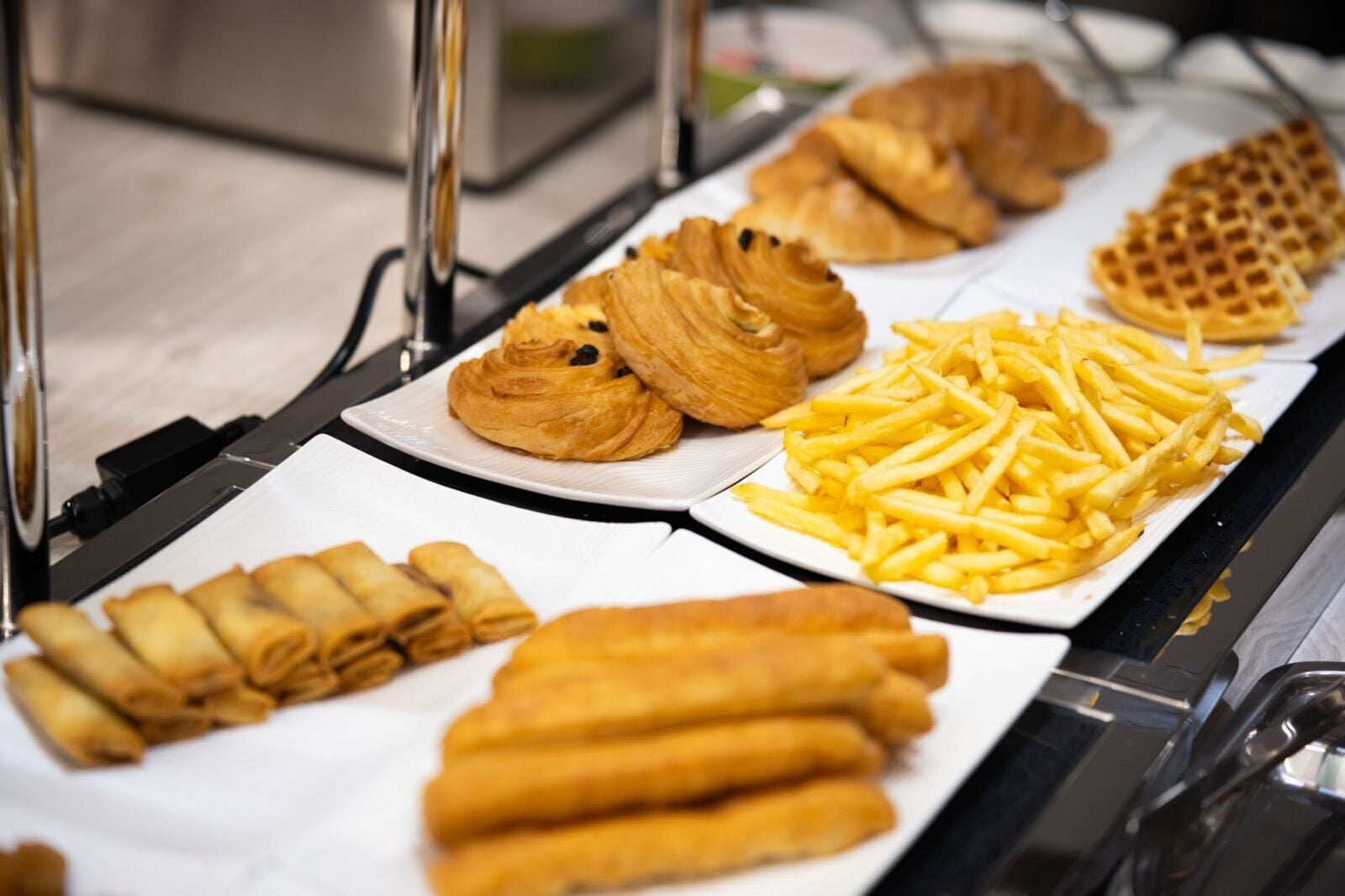 A buffet with various food items including pastries, croissants, and French fries.
