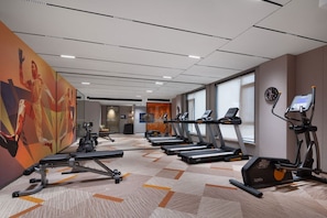 Un gimnasio con cintas de correr, elípticas y una pared con un mural abstracto grande.