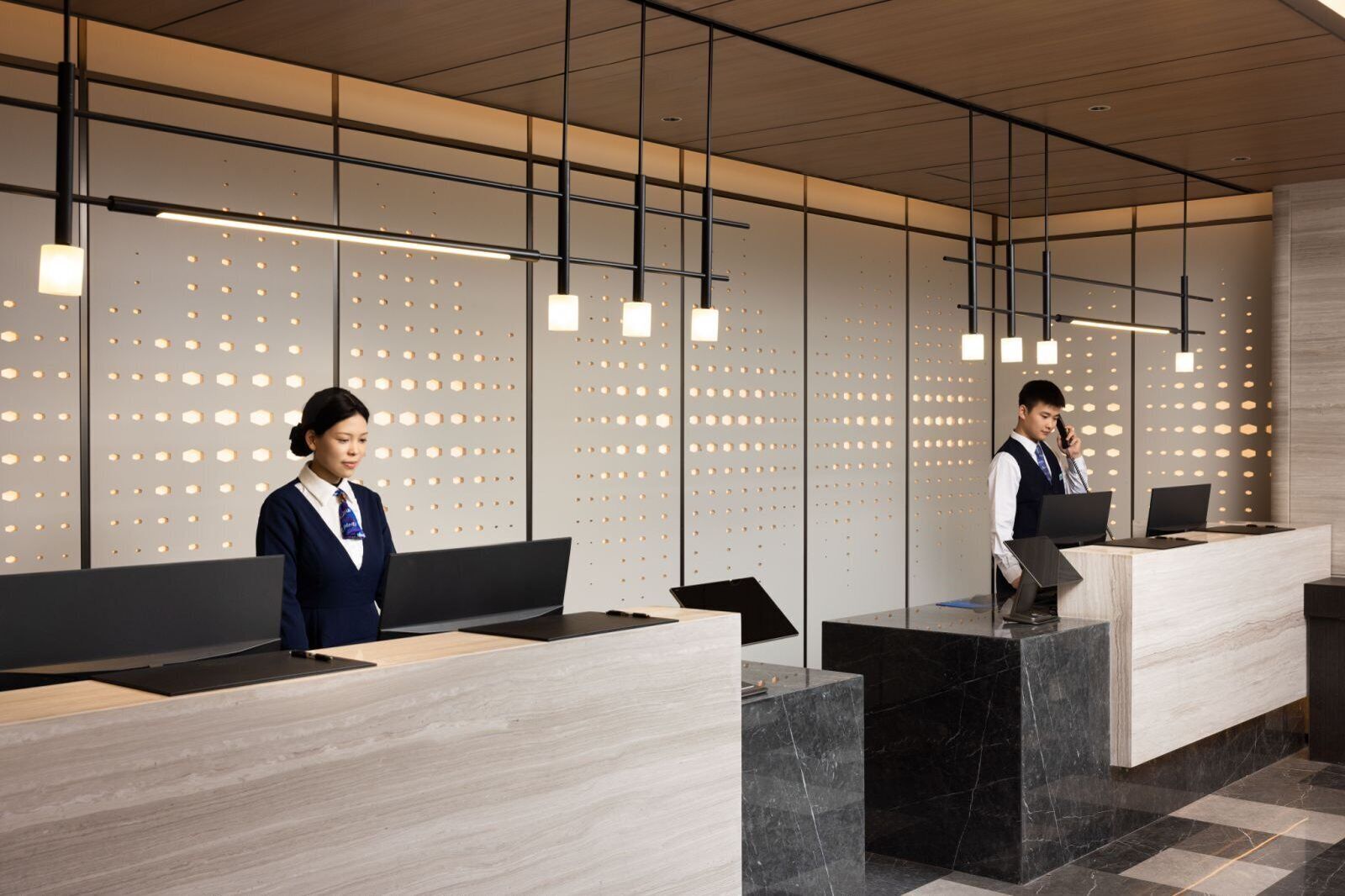 Una moderna recepción con una recepcionista y un huésped usando una computadora portátil.