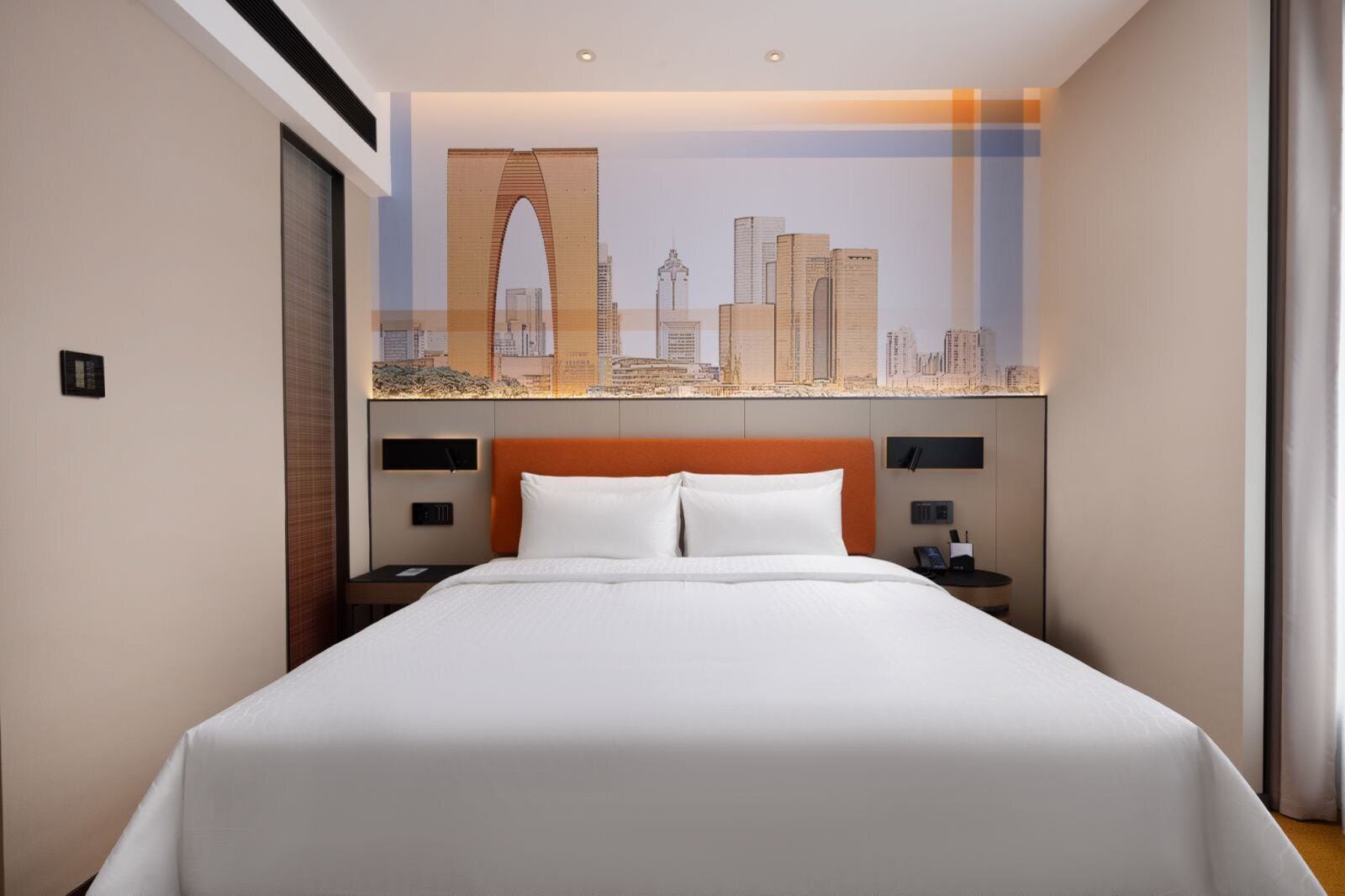 A hotel room with a large bed, a cityscape mural on the wall, and a modern headboard.