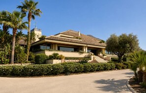Una casa a due piani con tetto in tegole, circondata da palme e un giardino curato.