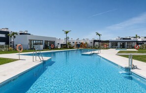 A swimming pool with clear blue water, surrounded by modern buildings, palm trees, and lifebuoys. - Modern Apartment in Habitat Estepona (Estepona)