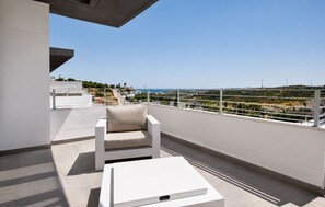 Uma varanda moderna com um sofá branco e uma mesinha, com vista para a paisagem costeira, incluindo edifícios e linhas de eletricidade.