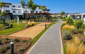A pathway leading to a building with a modern design, surrounded by landscaped gardens and a clear sky. - Modern Apartment in Habitat Estepona (Estepona)