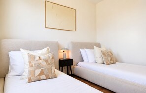 A hotel room with two beds, each with a headboard, a bedside table with a lamp, and a framed picture on the wall. - Modern Apartment in Habitat Estepona (Estepona)