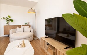 A modern living room with a sofa, a coffee table, a TV mounted on a wooden stand, a floor lamp, and a potted plant. - Modern Apartment in Habitat Estepona (Estepona)