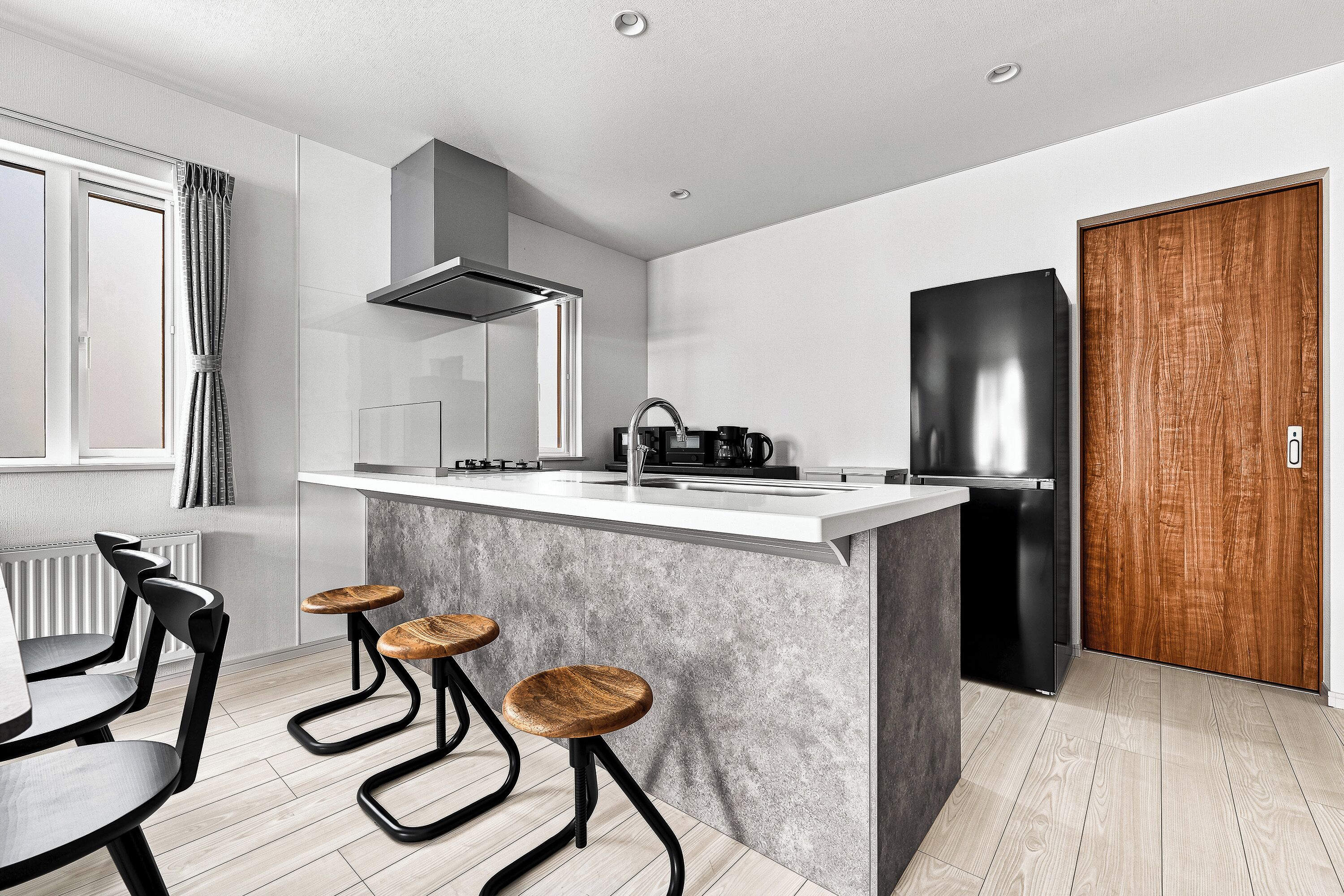 A modern kitchen with a central island, bar stools, a built-in oven, and a large refrigerator.