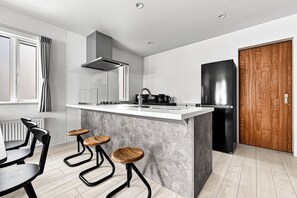 A modern kitchen with a central island, bar stools, a built-in oven, and a large refrigerator. - THE LORE II (Sapporo)