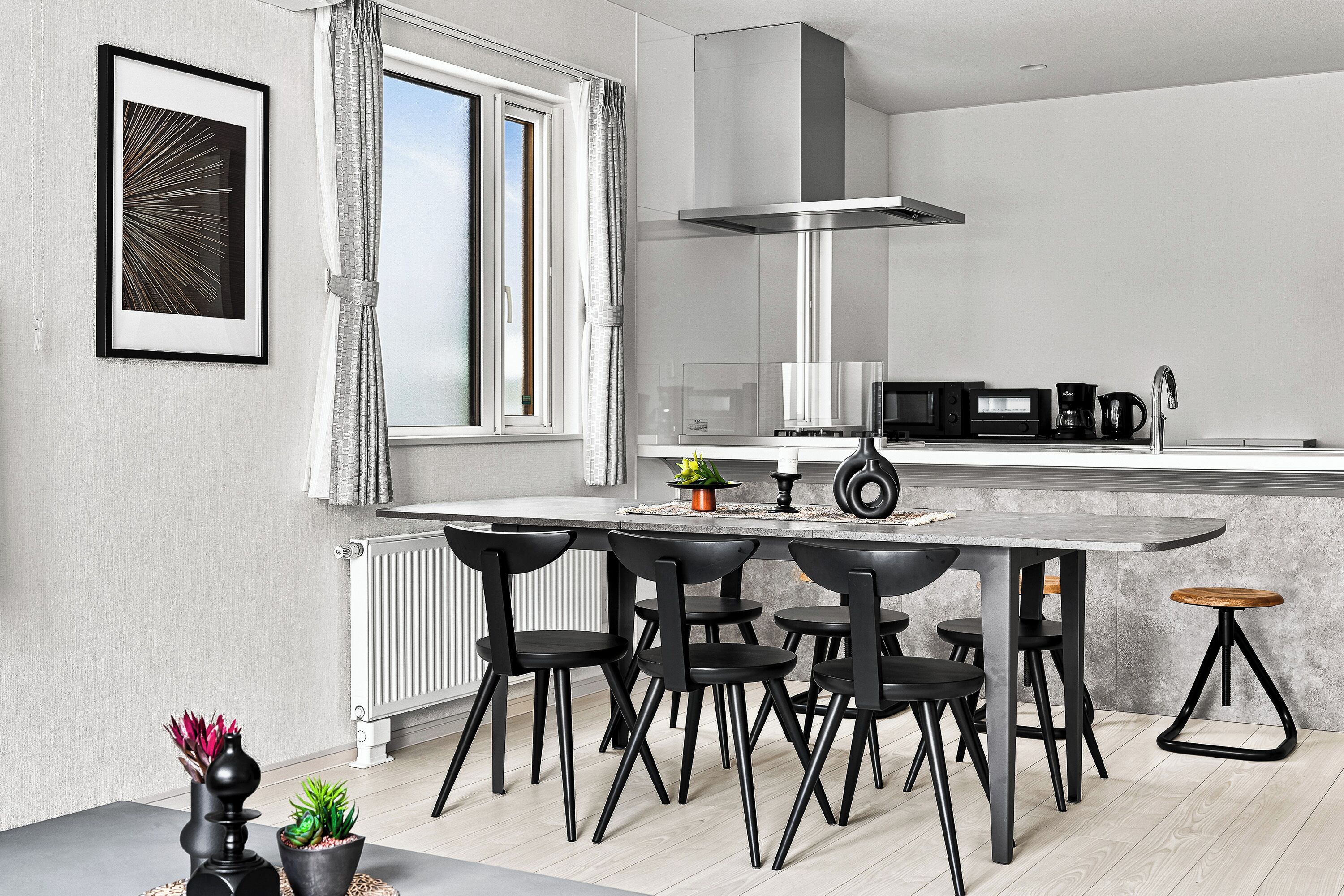 Una cocina moderna con comedor, que cuenta con un ventanal grande, un extractor de acero inoxidable y una cafetera.