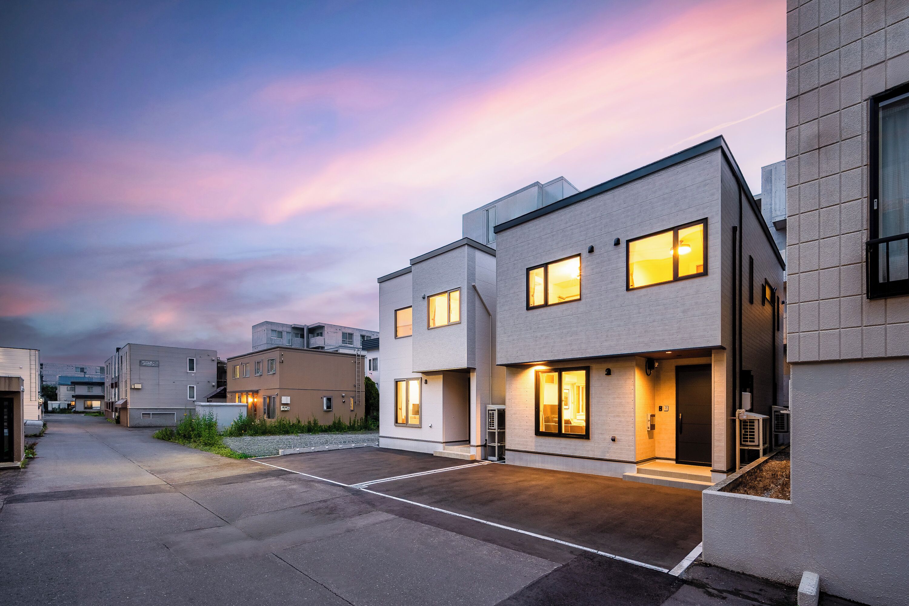 A modern residential building with multiple units, a paved driveway, and a clear sky.