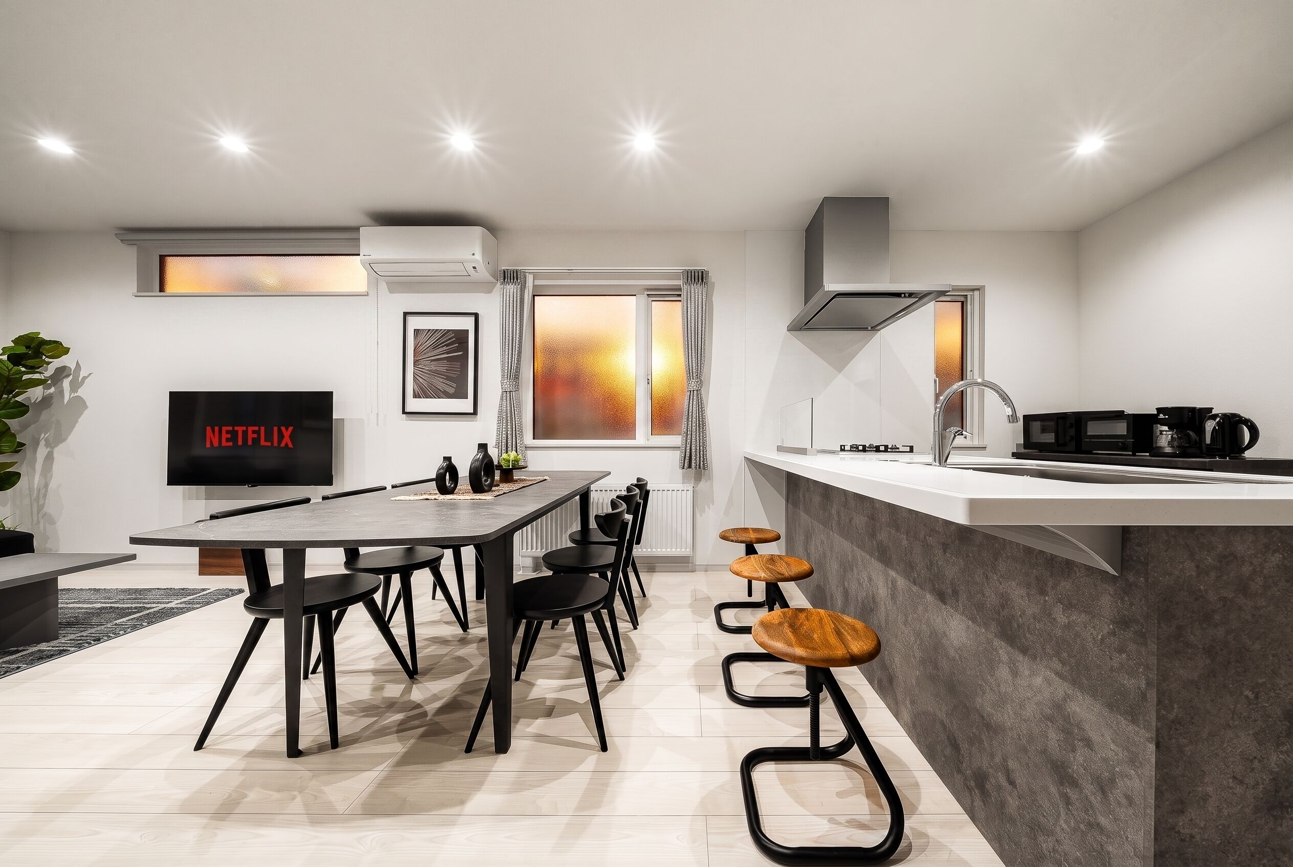 Cocina moderna con comedor, un televisor mostrando 'NETFLIX' y una ventana con vistas.