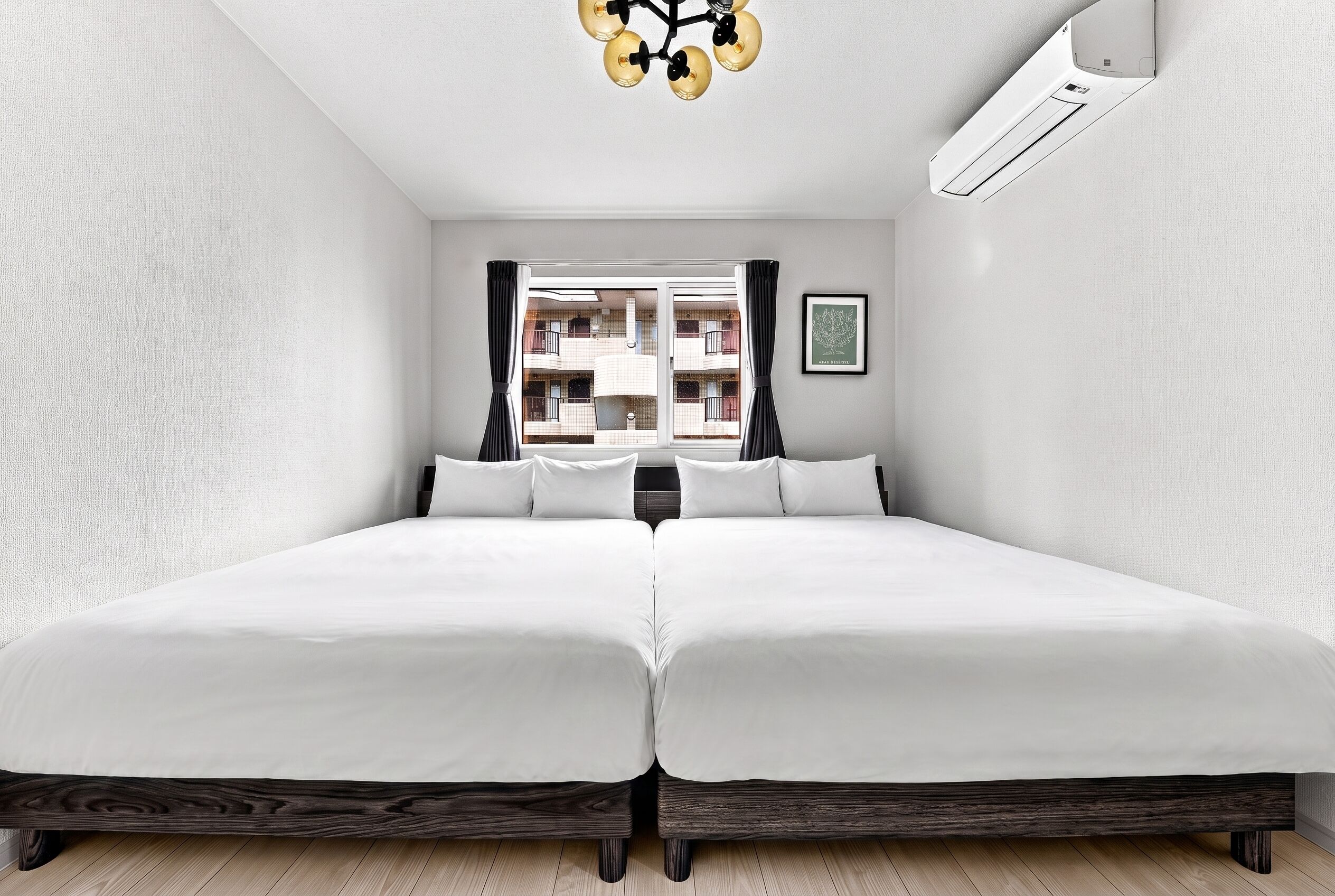 A double bed with a dark wooden frame, white bedding, and a view of a building through a window with curtains.