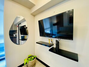 A modern living space with a mounted flat-screen TV, a circular mirror, and a potted plant. - Modern 2BR Coworking Yoga Studio WiFi (San Isidro)
