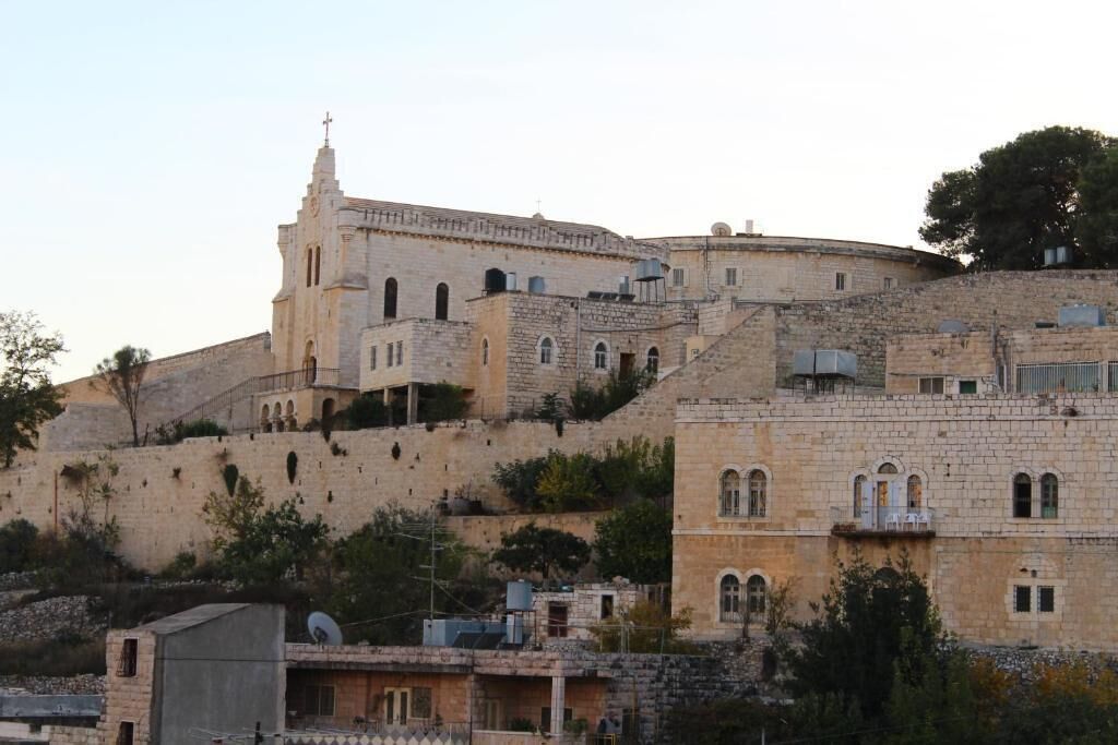A historic stone building with a prominent bell tower, multiple windows, and a fortified wall.