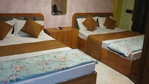 Une chambre d’hôtel avec deux lits en bois, chacun recouvert d’une courtepointe à motifs floraux, une petite armoire en bois et un miroir au mur.