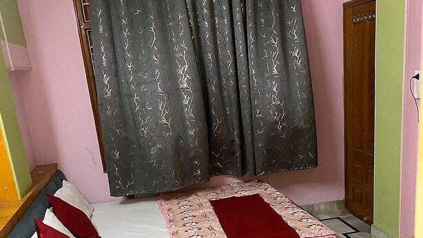 Une chambre à coucher avec un lit, des oreillers, un tapis rouge et une fenêtre avec des rideaux.