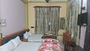 Une chambre avec deux lits, un ventilateur de plafond, une télévision et des rideaux.