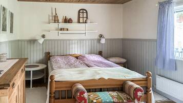 Une chambre à coucher avec un lit en bois, une table de chevet, une petite table ronde, une étagère avec des objets décoratifs et une fenêtre avec des rideaux.