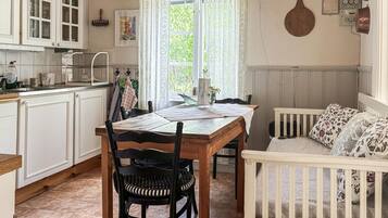 Une cuisine avec des meubles blancs, une table à manger avec des chaises et un berceau avec du linge de lit à motifs floraux.