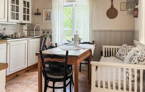 Una cocina con armarios blancos, una mesa de comedor con sillas y una cuna con ropa de cama floral.