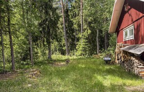 Un edificio de madera roja con cimientos de piedra, rodeado por un bosque frondoso.