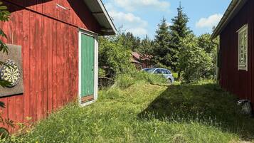 Un bâtiment en bois rouge avec une porte verte, une voiture garée à l’arrière-plan et une zone herbeuse avec des arbres.