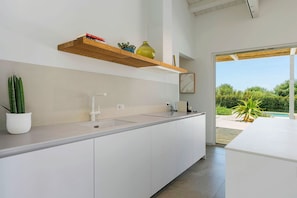 Une cuisine moderne dotée d’un îlot central intégré, d’une étagère suspendue au-dessus du plan de travail et offrant une vue sur une piscine à l’extérieur.