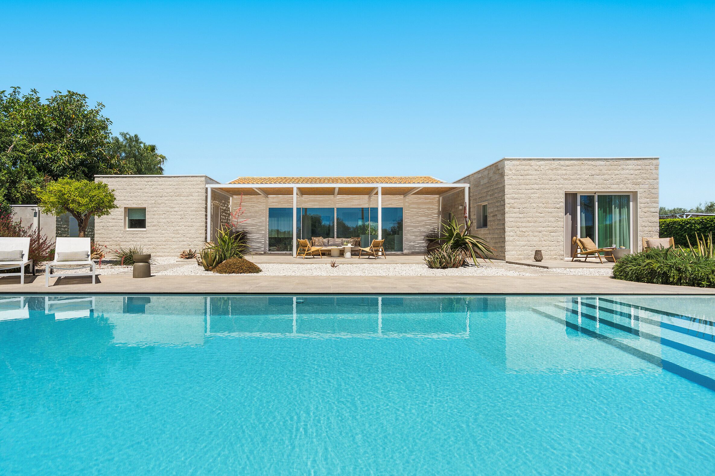 Una casa moderna con piscina, un patio cubierto y jardín.