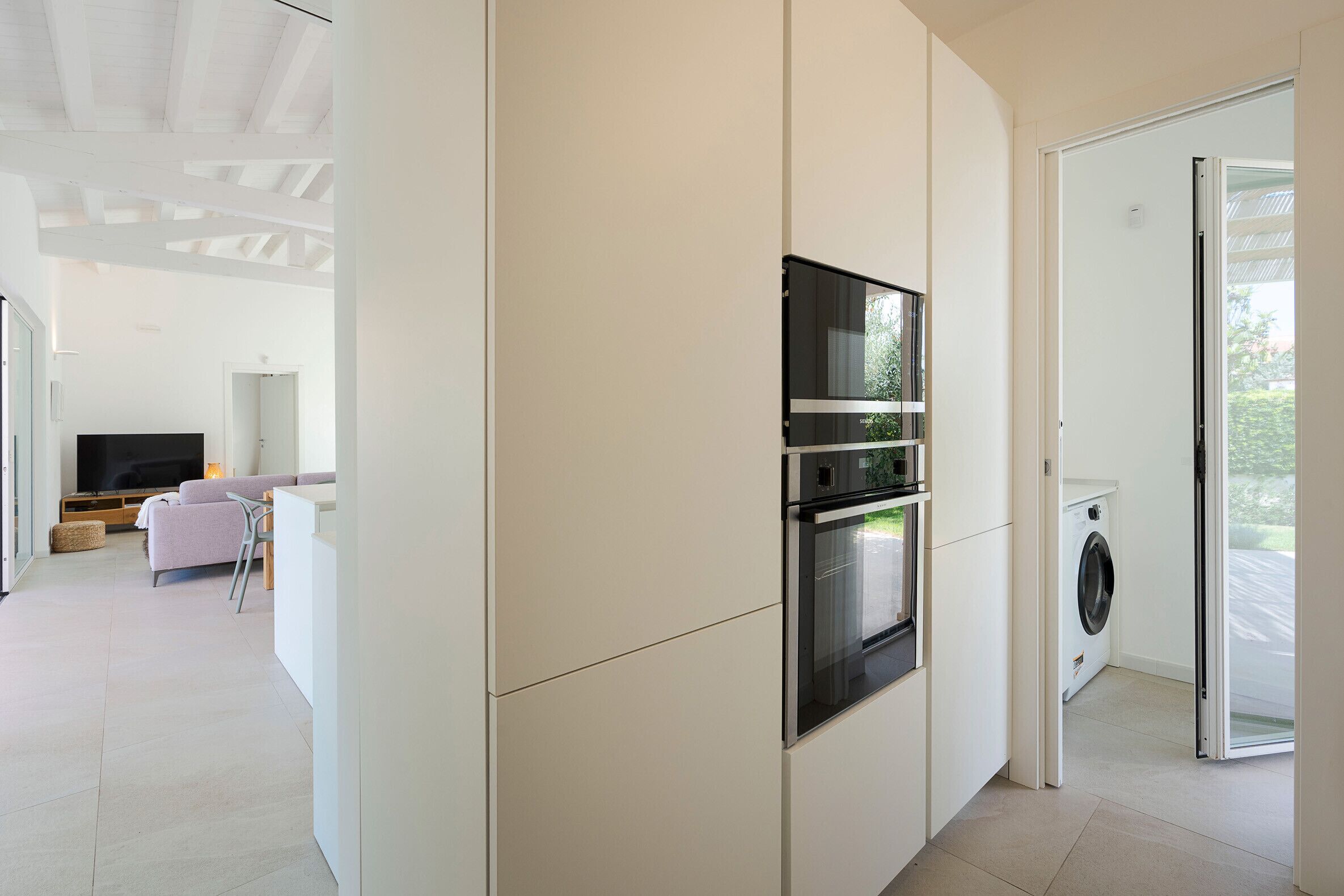 Une cuisine moderne dotée d’appareils électroménagers intégrés, un coin repas avec un canapé et une table, et une vue sur l’extérieur.