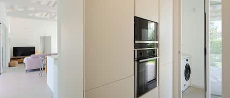 Una cocina moderna con electrodomésticos integrados, una zona de comedor con sofá y mesa, y vistas al exterior.