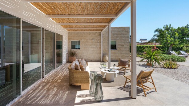 A covered outdoor seating area with wicker furniture, a glass wall, and a stone wall. - Beautiful villa with private pool in Fontane Bianche - DiCasaInSicilia (Fontane Bianche)