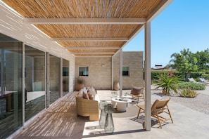 A covered outdoor seating area with wicker furniture, a glass wall, and a stone wall. - Beautiful villa with private pool in Fontane Bianche - DiCasaInSicilia (Fontane Bianche)