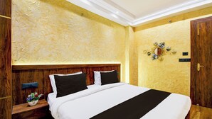 A hotel room with a large bed, wooden headboard, a nightstand with a lamp, and a decorative wall piece. - Super Hotel O Prayagraj Junction (Prayagraj)