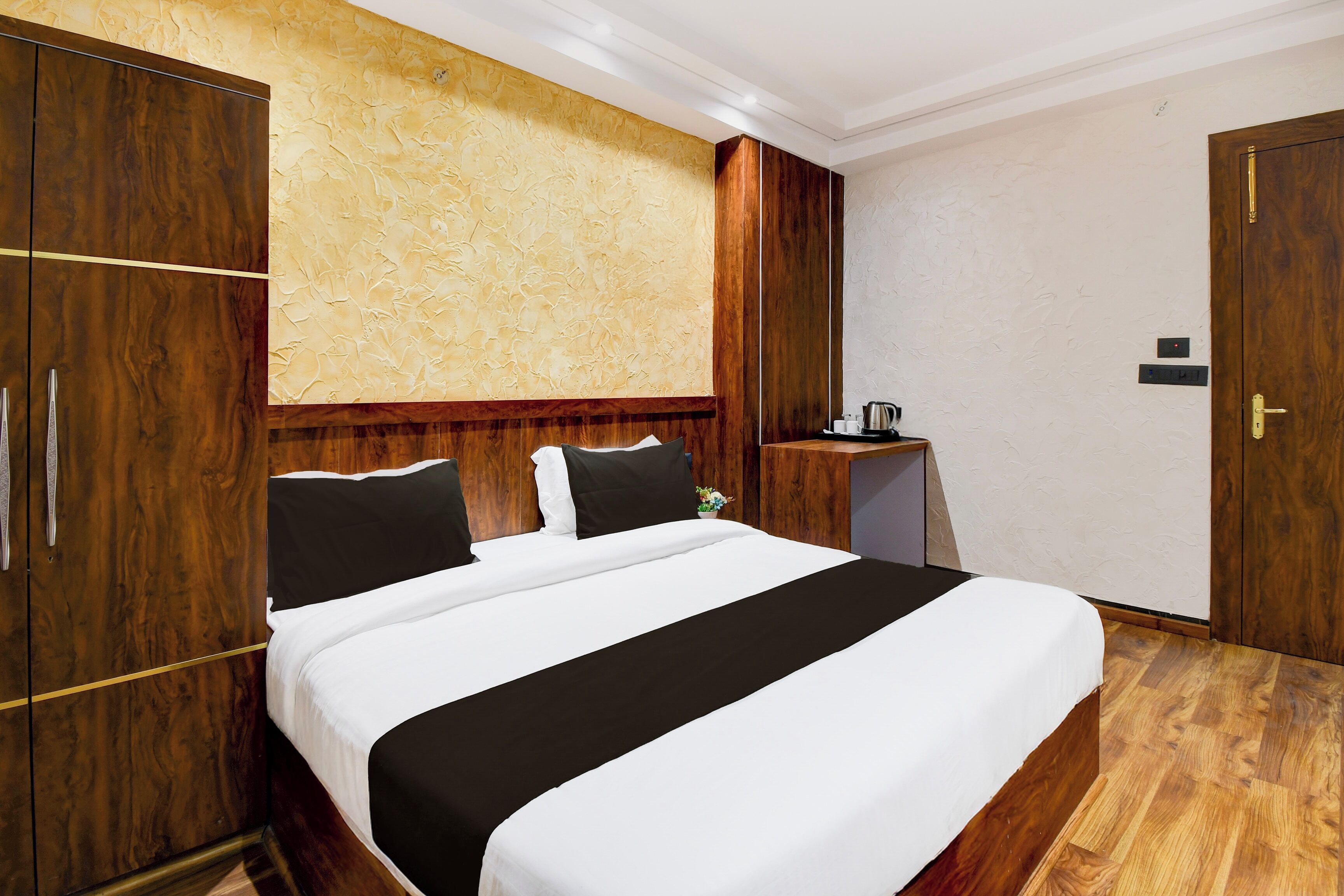 Habitación de hotel con una cama grande, un armario de madera, una mesita de noche con una tetera y una puerta con cerradura.