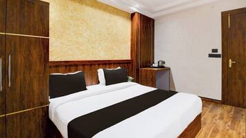 Habitación de hotel con una cama grande, un armario de madera, una mesita de noche con una tetera y una puerta con cerradura.