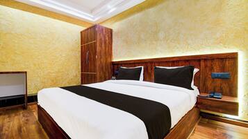 Une chambre d’hôtel avec un grand lit, une tête de lit en bois, une armoire, une table de chevet avec un téléphone et un luminaire fixé au mur.