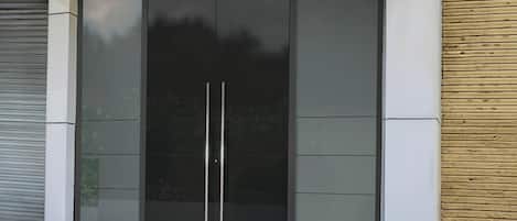 A modern building facade with a large glass door and a wooden panel on the right.