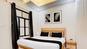 Quarto de hotel com cama, mesa de cabeceira, abajur e duas obras de arte emolduradas na parede.
