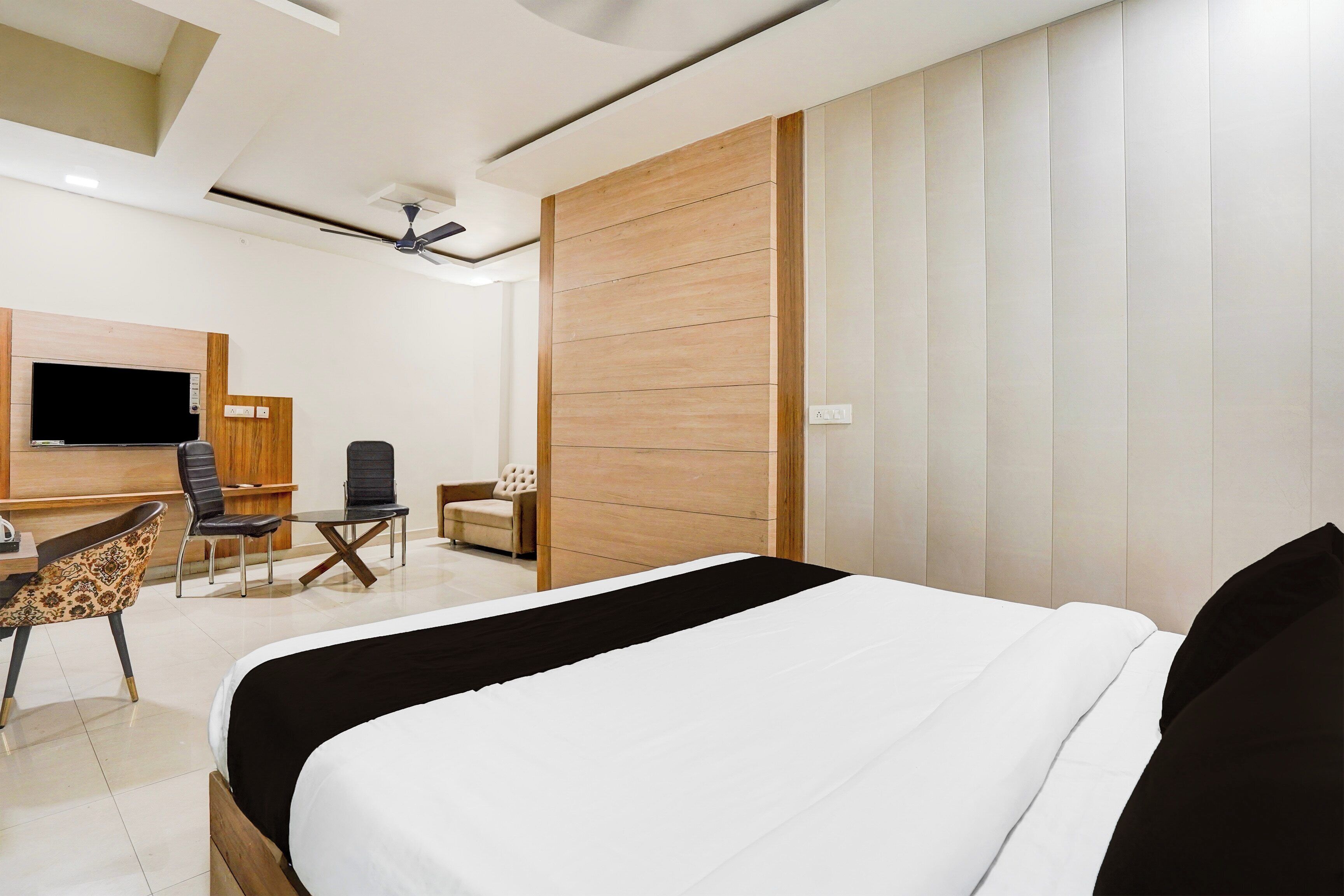 Une chambre d’hôtel moderne, dotée d’un grand lit, d’un bureau avec une chaise, d’un canapé et d’un téléviseur fixé au mur.