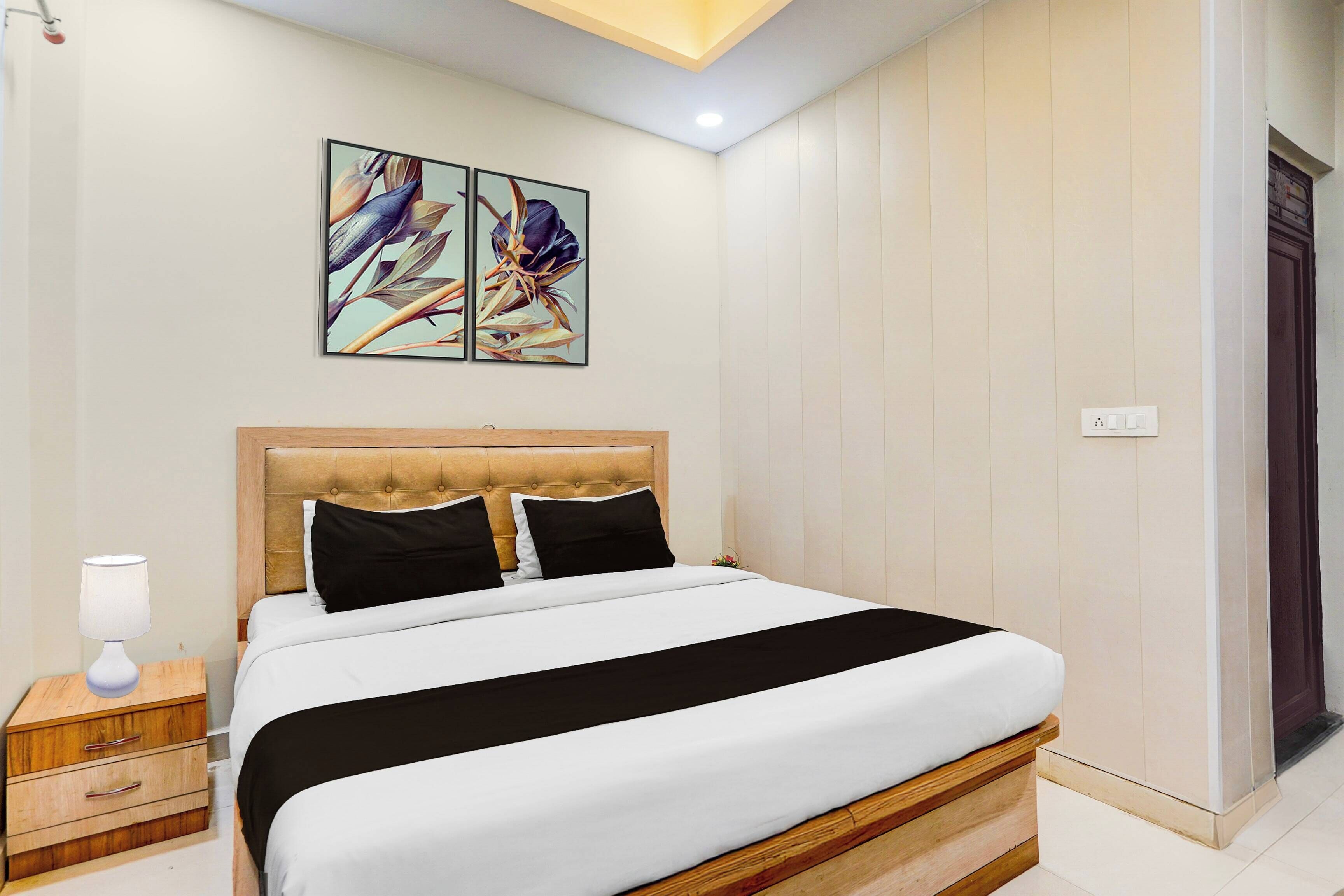 A hotel room with a bed, bedside table, lamp, and artwork on the wall.