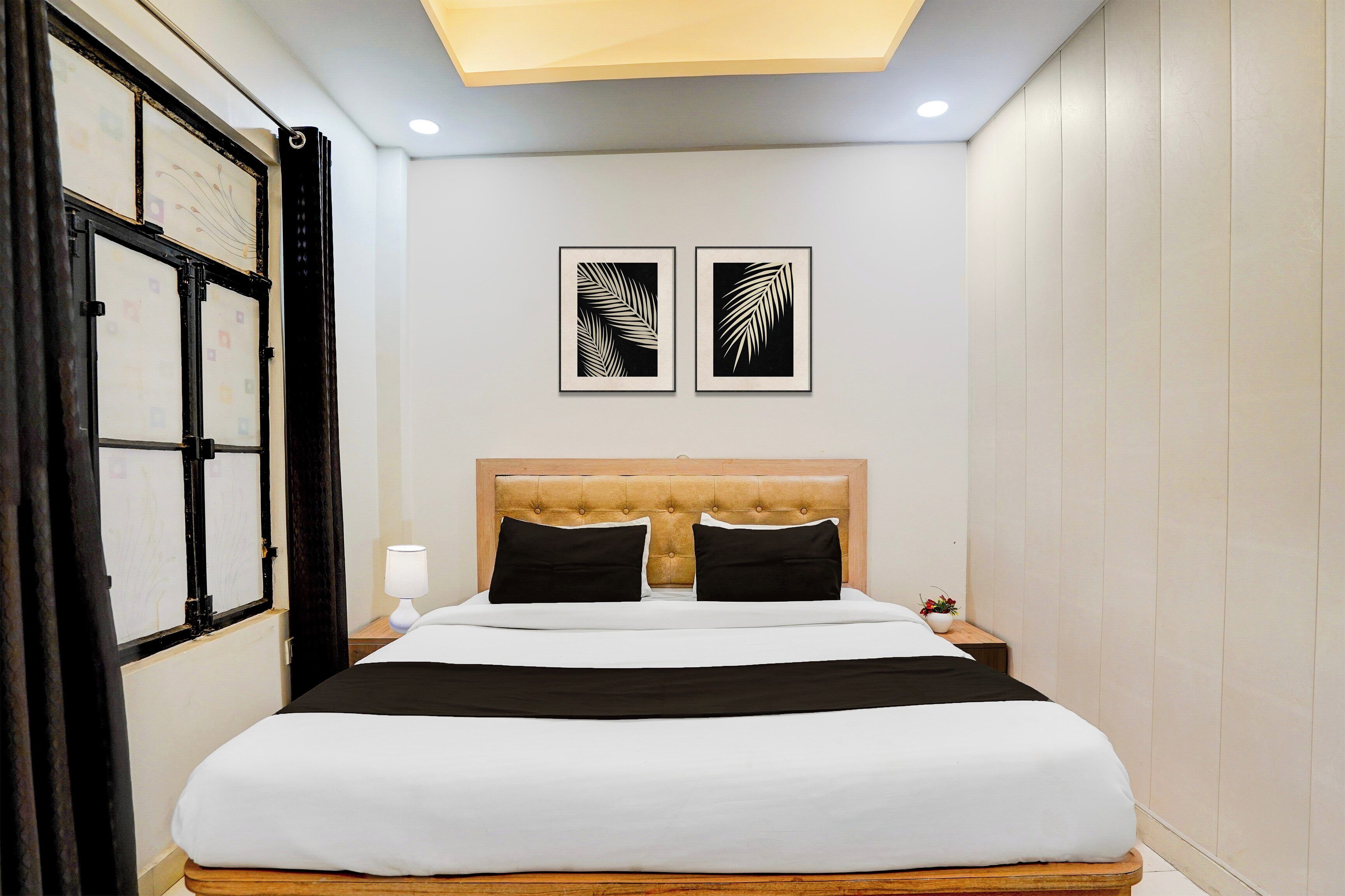Habitación de hotel con cama, mesita de noche, lámpara y dos diseños de hojas enmarcadas en la pared.
