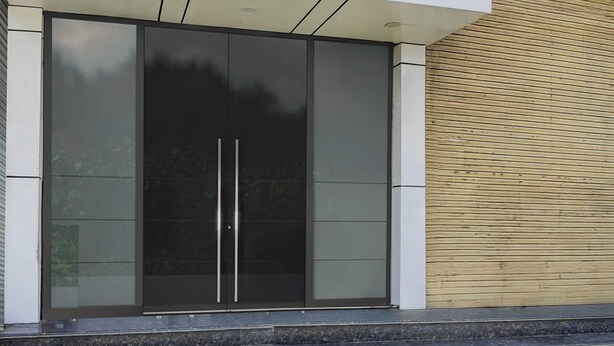 Entrada de um edifício moderno com porta de vidro e painel de parede de madeira.